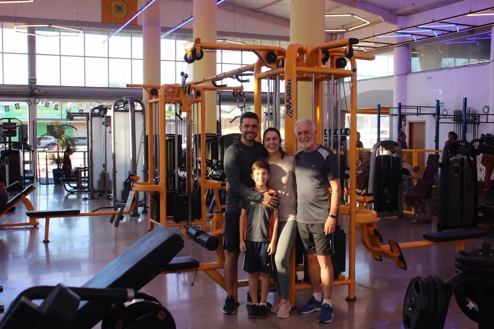 Família treinando na Yellow Fit: pai, mãe, filho e avô juntos na área de musculação